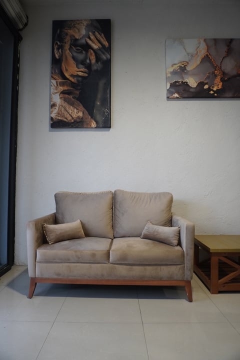 Beige two-seater sofa with wooden legs in a minimalist room with abstract artwork on white walls