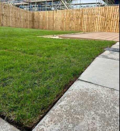 Landscaped backyard with artificial turf grass, concrete patio, wooden fence, and construction site in background