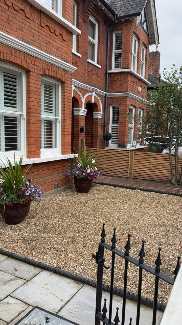 Red brick Victorian house exterior with gravel courtyard, planters, and black iron fence