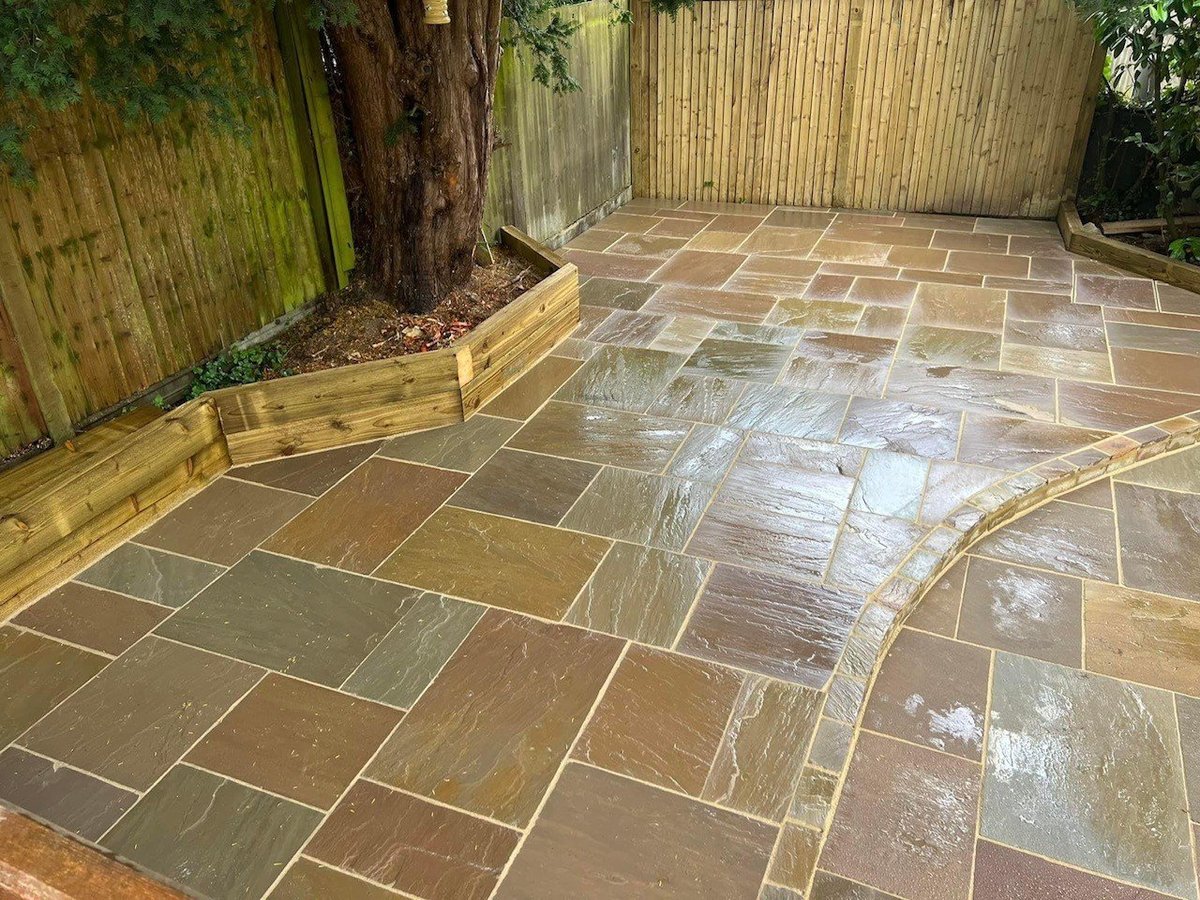 Newly laid natural stone patio with herringbone pattern in a backyard, surrounded by wooden fencing and garden beds