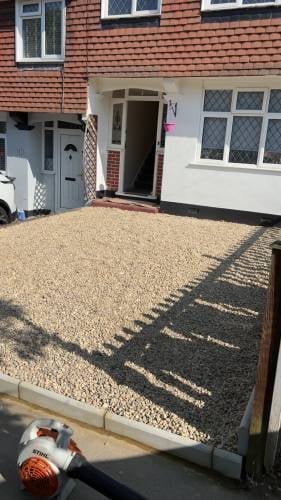 Residential driveway with gravel surface and door mat at entrance to brick townhouse with white windows and trim