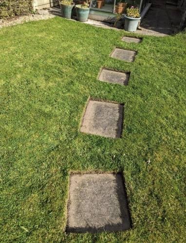 Stone stepping stones leading diagonally across a green lawn toward a patio area