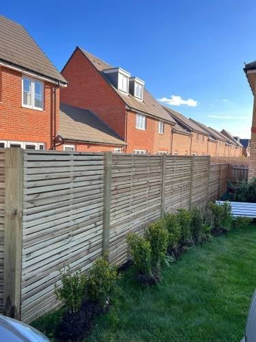 Wooden fence bordering residential brick homes with green lawn and clear blue sky