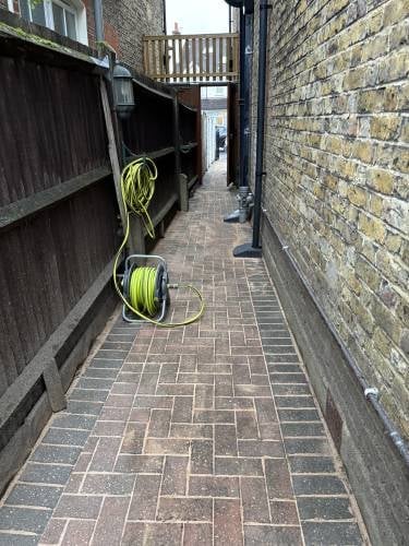Narrow alleyway between brick walls with coiled yellow garden hoses on herringbone patterned pavement