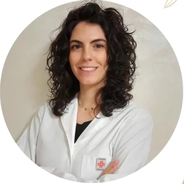 Ritratto di una donna con lunghi capelli scuri ricci che indossa un camice bianco con stetoscopio, su sfondo beige circolare