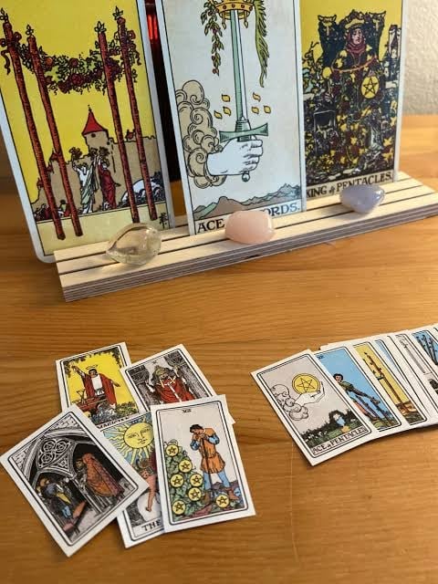 Tarot cards displayed on wooden table, with card holder showing multiple cards including Eight of Cups, Ace of Swords, and King of Pentacles in background