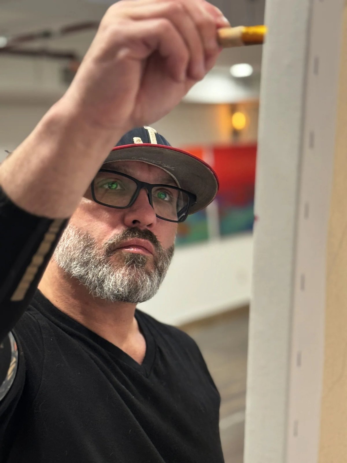 Man with beard and glasses holding a cigar, wearing a black cap and black shirt