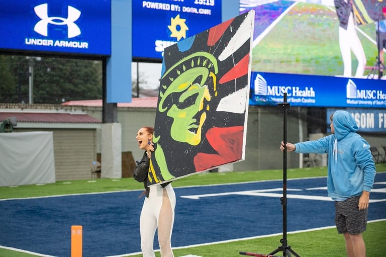 Female athlete holding large yellow and red flag on blue field with stadium signage and another person visible in background