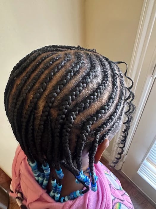 Back view of a child with cornrow braids in neat rows, decorated with blue beads at the ends, wearing a pink shirt