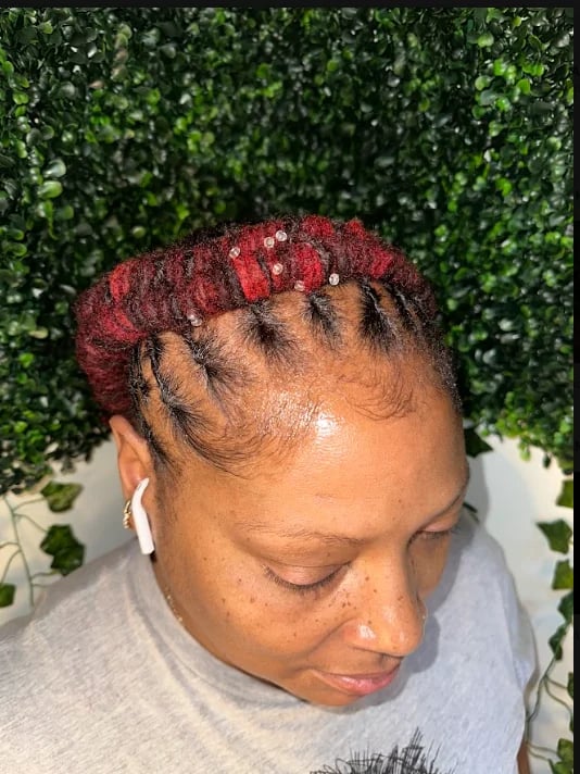 Top profile of a person with burgundy locs accented with shimmering gold beads, against a green leafy background