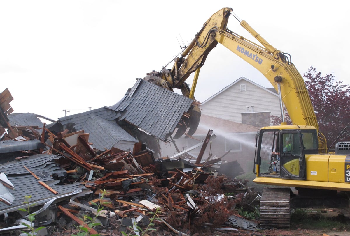 Yellow excavator with raised bucket demolishing metal structure and scrap materials at recycling or demolition site