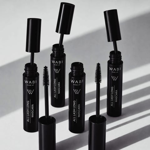 Five black Wabi mascara bottles with brushes arranged on a white surface with dramatic shadows