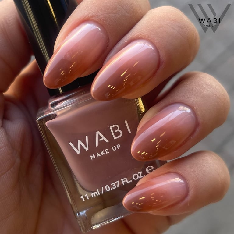 Manicured hand holding WABI Make Up nail polish bottle with warm brown gradient nail polish applied