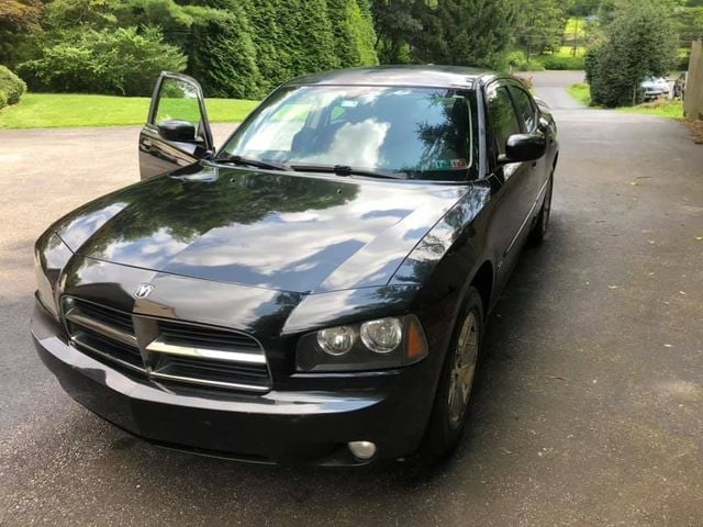 Black Dodge Charger sedan parked in a driveway, driver's side door open, green hedges behind