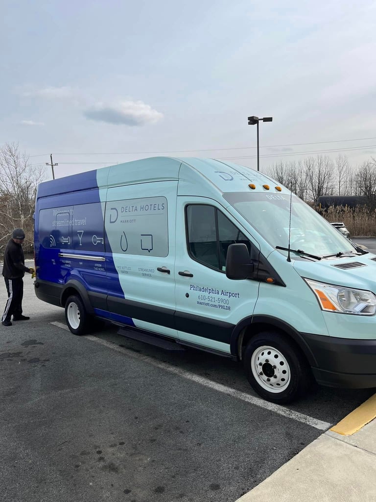 Light blue and navy Delta Hotels shuttle van parked in a lot with bare trees in the background