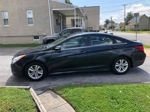 Black sedan parked on a residential street in front of a house with a lawn