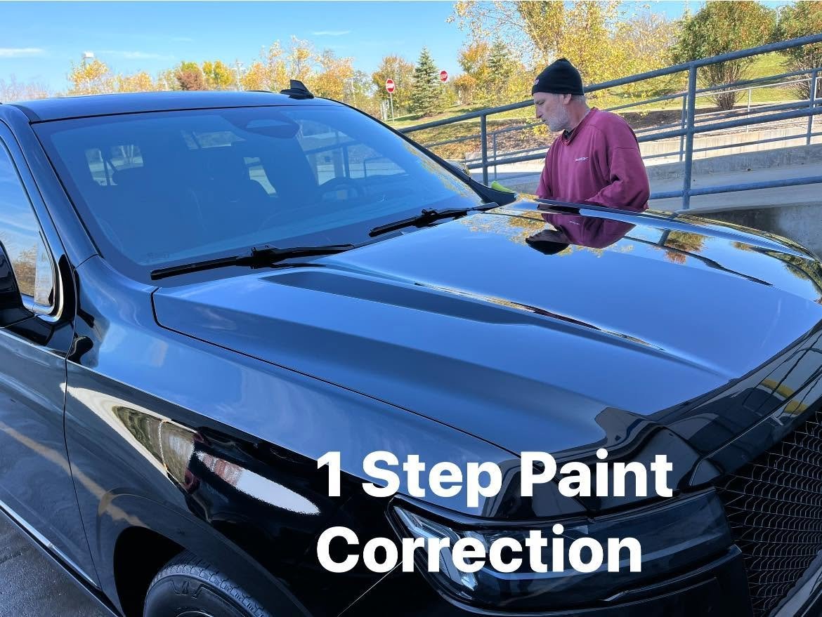 Detailer applying a one-step paint correction to a black truck hood with a buffing pad at an outdoor location with fall foliage