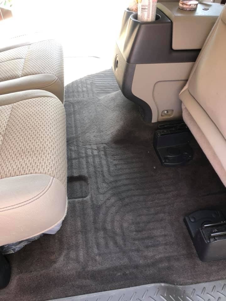 Interior view of a vehicle showing the back seat area with two-tone upholstery and a gray floor mat