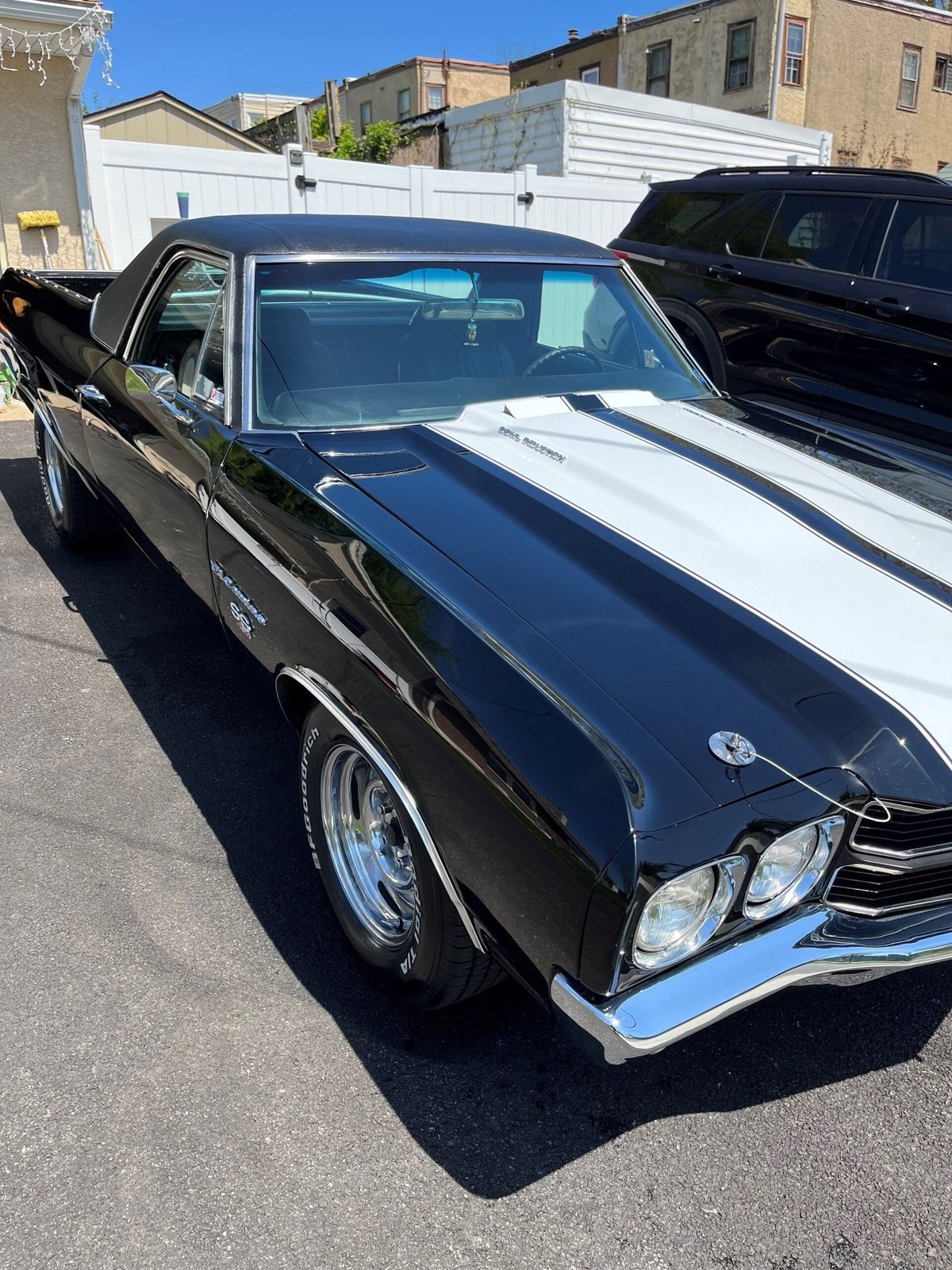 Black and white classic 1970s muscle car with white racing stripes parked on the street