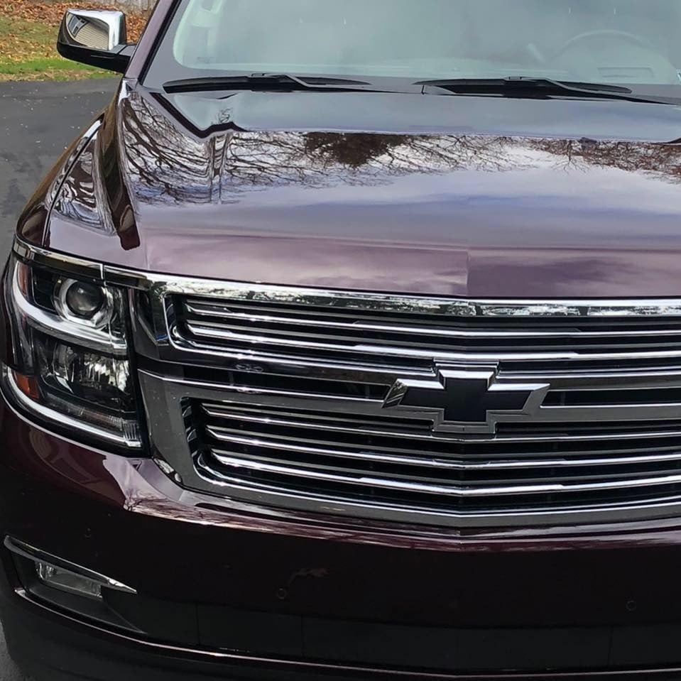 Reflective close-up of a maroon Chevrolet SUV grille, headlights and hood after exterior detailing