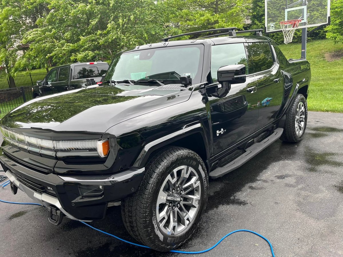 Black GMC Hummer EV pickup truck with a glossy finish parked in a driveway with a green lawn and basketball hoop behind