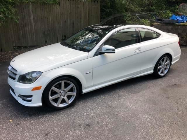 White Mercedes-Benz C-Class coupe with silver alloy wheels parked on a residential driveway
