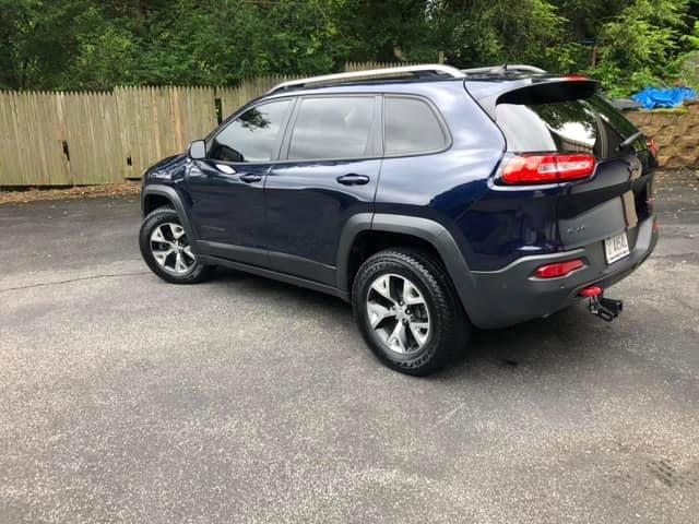 Dark blue Jeep Cherokee SUV parked on a driveway with a wooden fence and trees behind