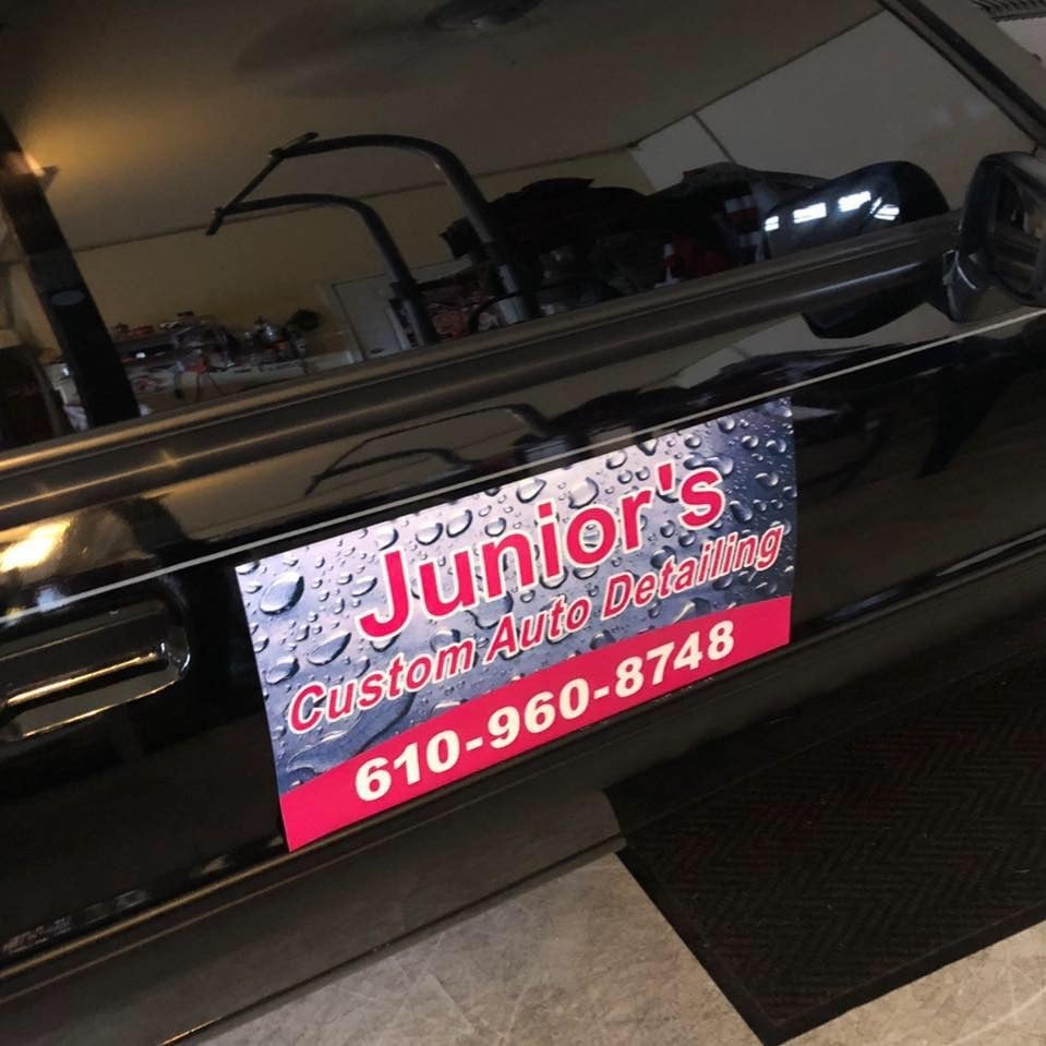 Illuminated Junior's Custom Auto Detailing sign with phone number 610-960-8748 on a black vehicle door