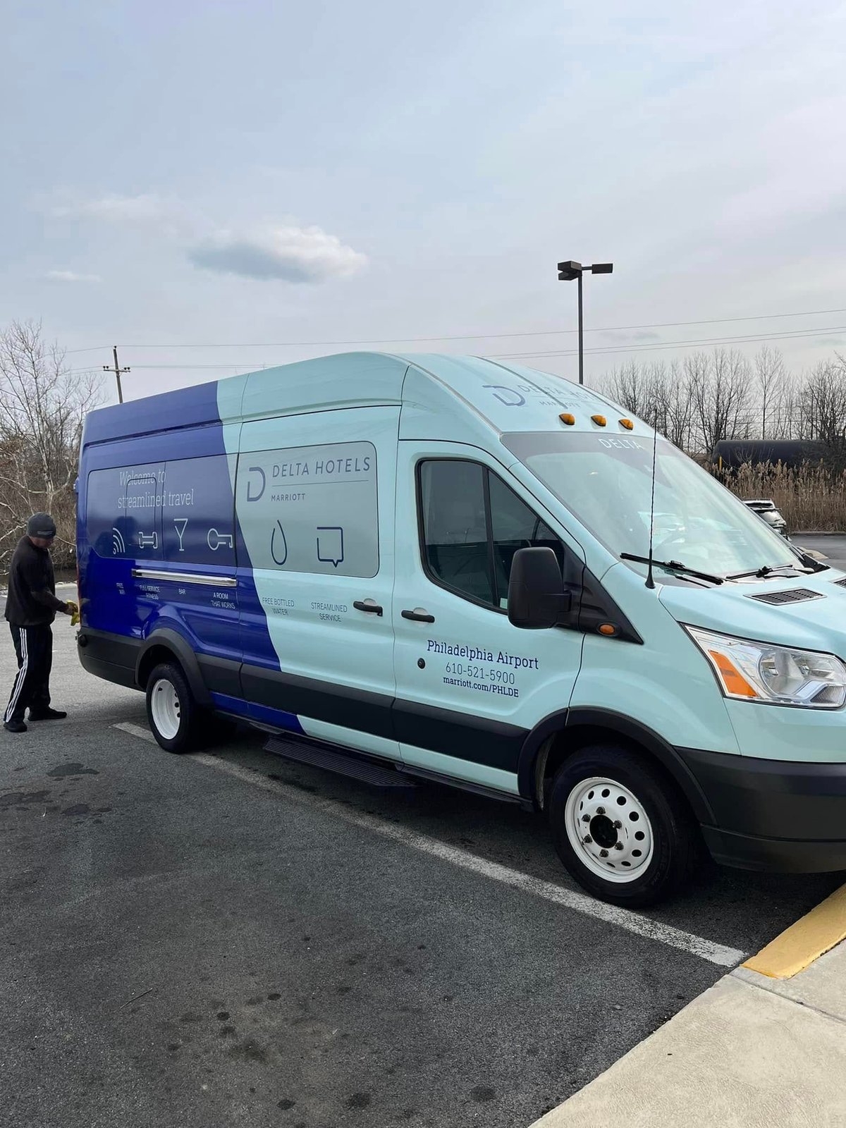 Light blue and dark blue Delta Hotels Marriott branded shuttle van parked on asphalt after detailing