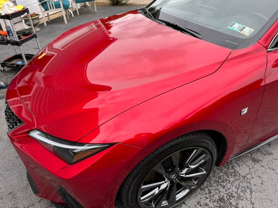 Red Lexus sports car with the hood open in a parking lot, showing a glossy hood and alloy wheels after detailing