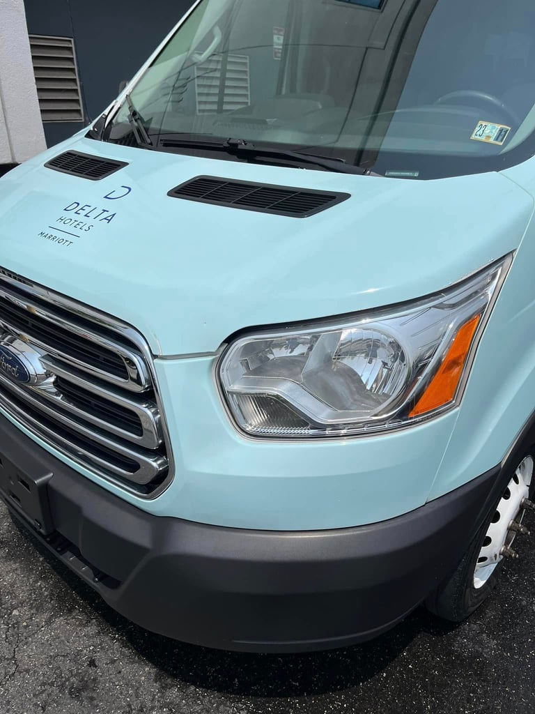 Light blue commercial delivery truck front view showing hood vents, headlight, and grille detail in parking lot