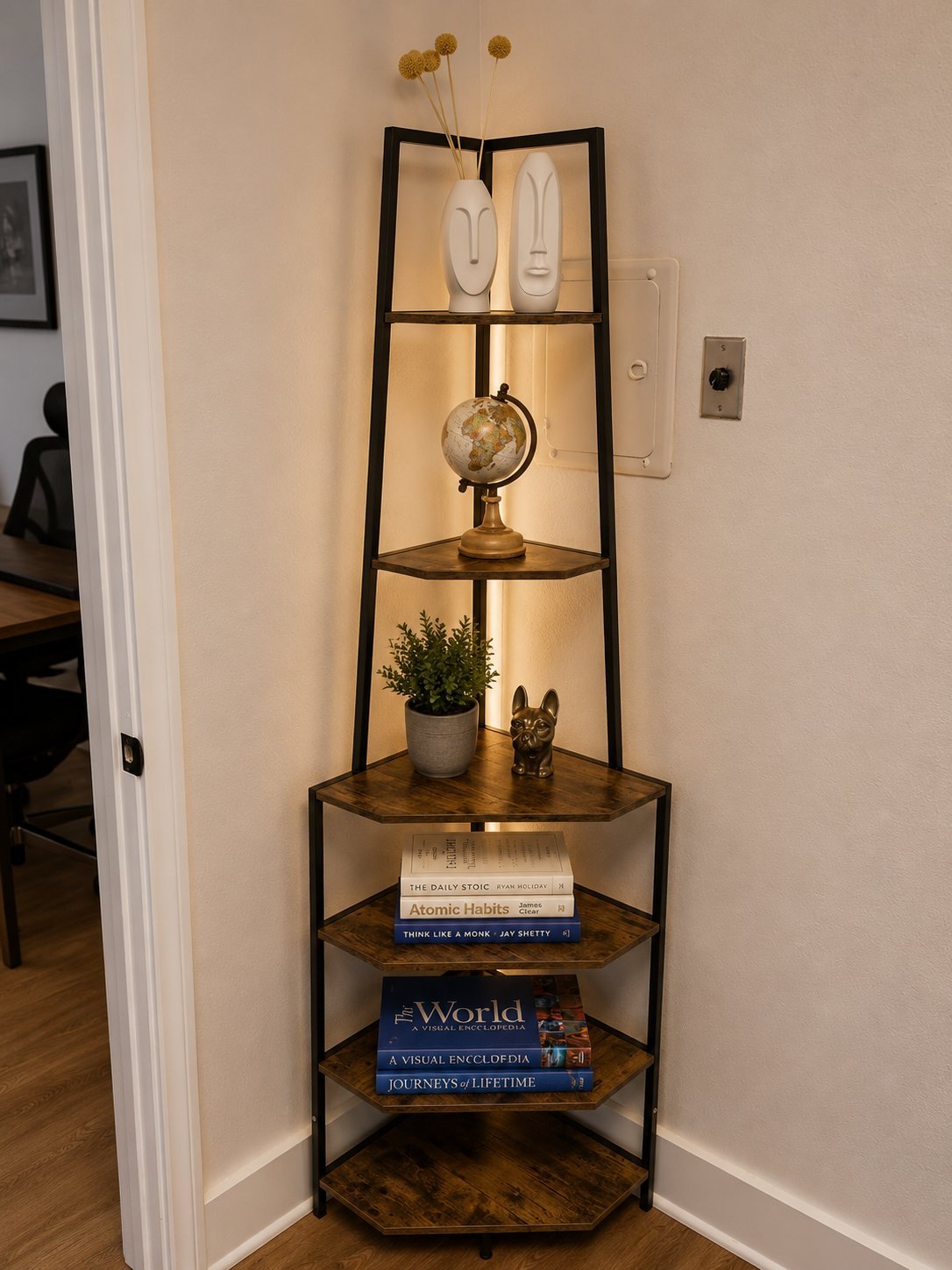 Tall corner shelf unit with wooden shelves displaying books, potted plant, globe, and decorative items against beige wall