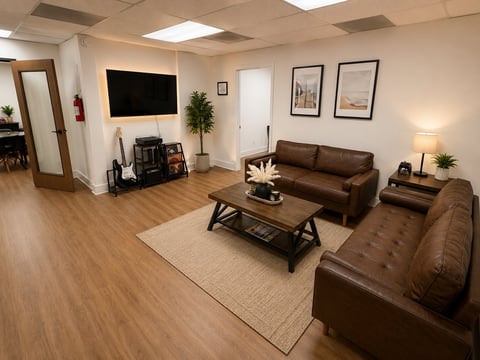 Modern basement living room with brown leather furniture, flat-screen TV on wall, wooden coffee table, and warm lighting