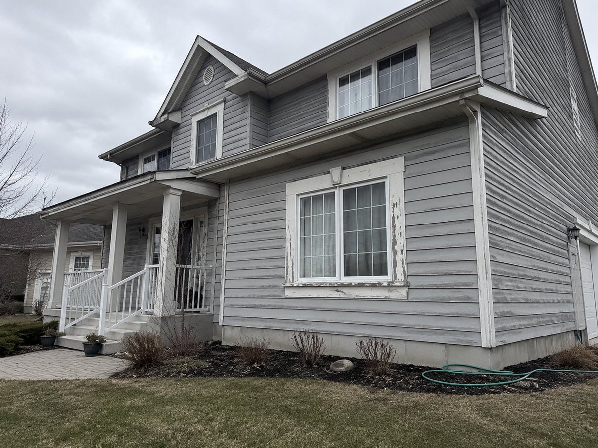 Two-story gray home before repainting — weathered horizontal siding with peeling paint around the window trim, front porch, and bay window