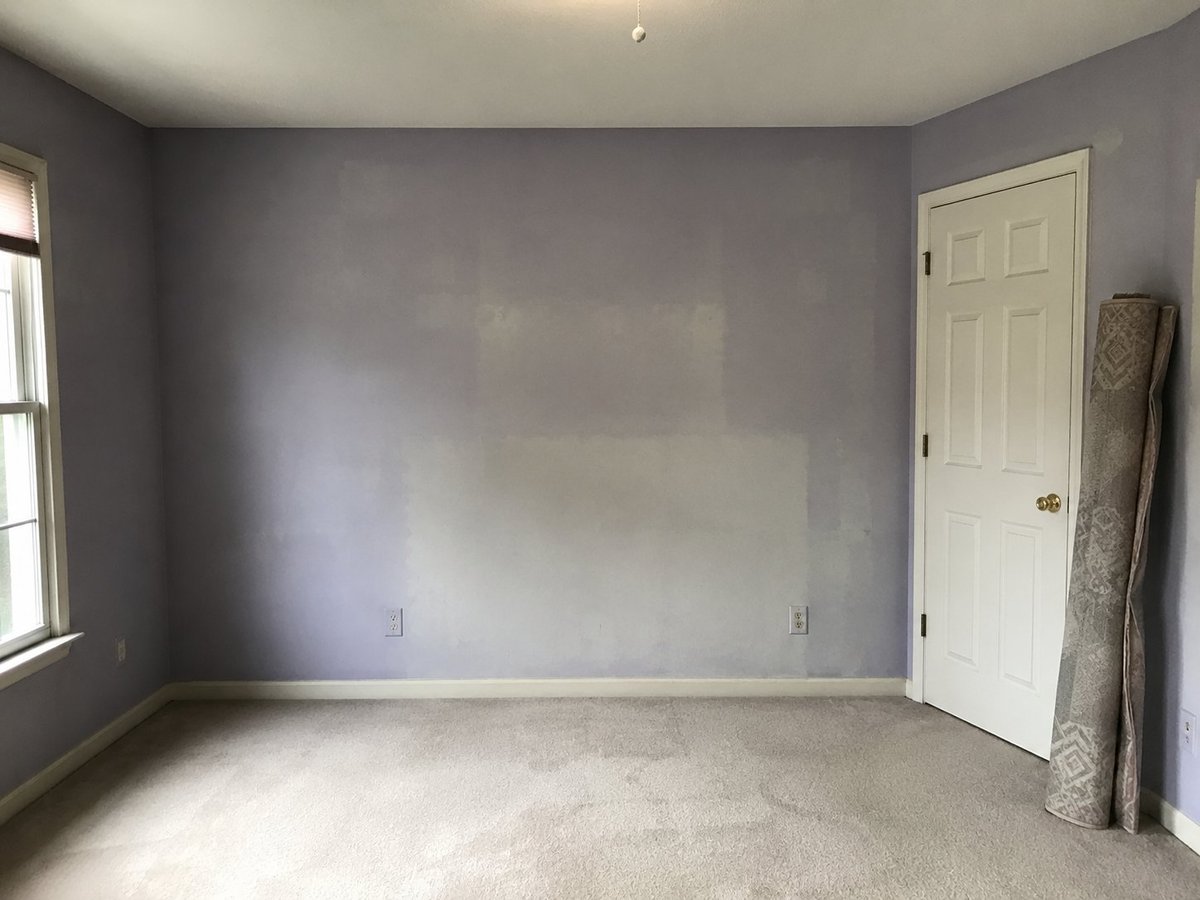 Empty bedroom after painting — freshly painted lavender walls, beige carpet, window and closet door