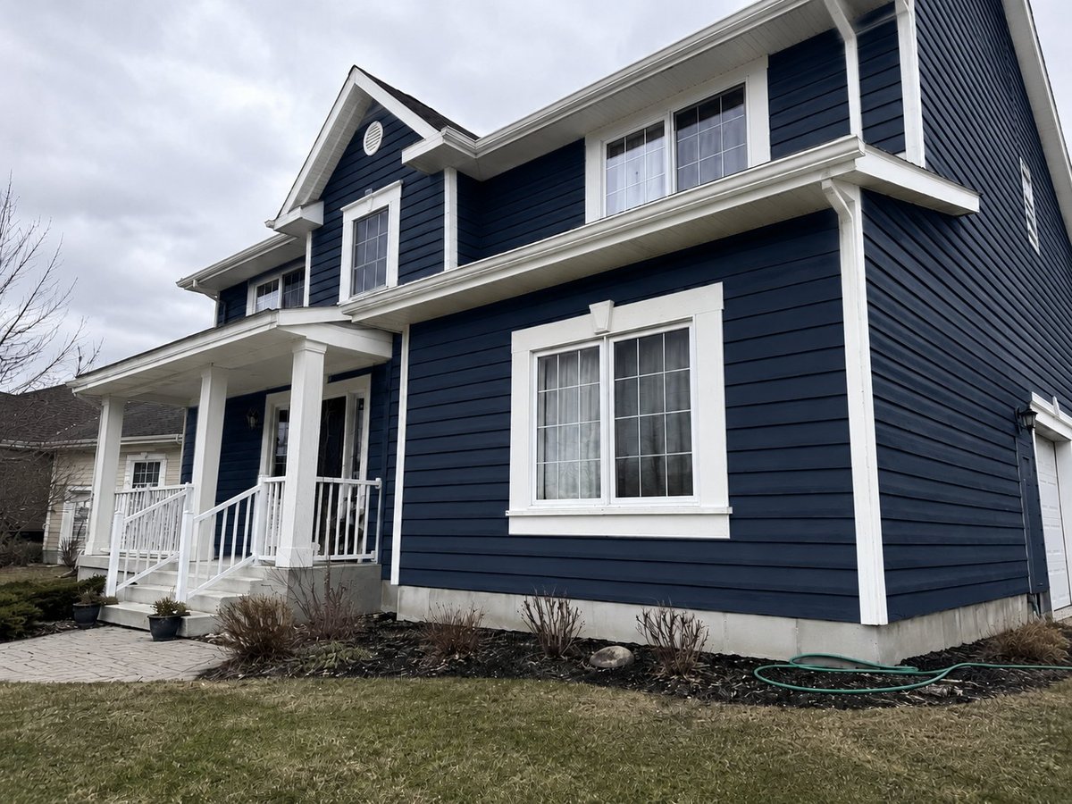 Two-story home after repainting — deep navy blue siding with crisp white trim, white front porch railings, and gabled roof — Ottawa exterior refresh