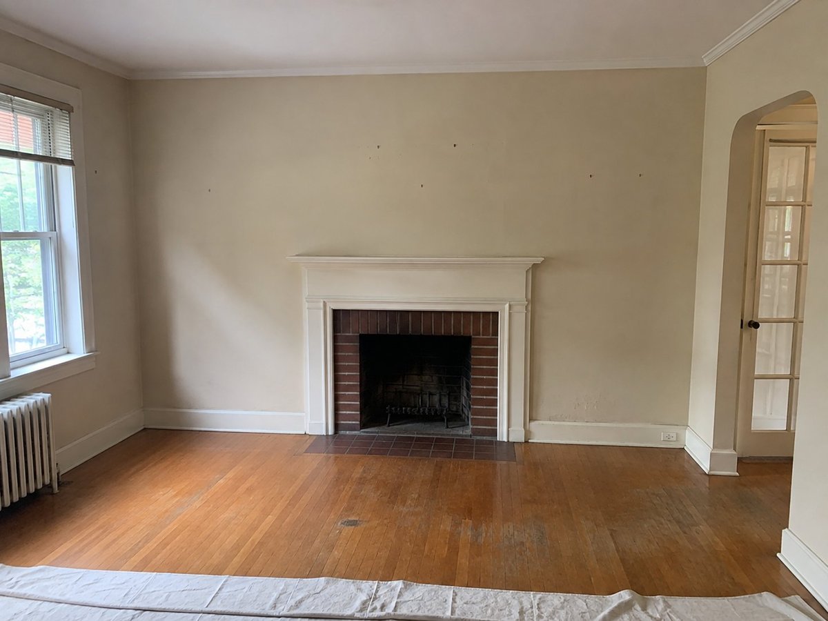 Living room before painting — walls with visible scuffs and marks, hardwood floors, white fireplace with brick interior