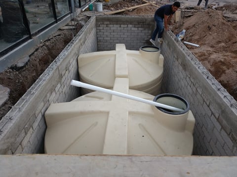 Two large cream-colored septic tanks installed in a concrete underground pit