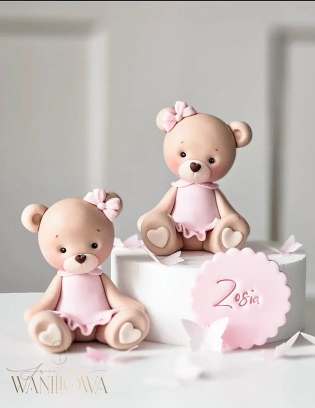 Two fondant teddy bears in pink dresses with pink bows on a white tiered cake decorated with Zosia name tag