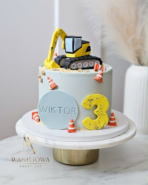 Yellow toy excavator on a tiered construction-themed birthday cake with number 3, traffic cones, and Wiktor text