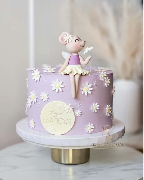 Purple tiered cake decorated with white daisies and topped with a fondant fairy figurine in pink and purple dress