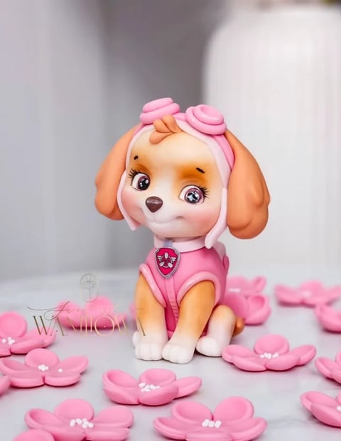 Pink and orange toy dog figurine with bows surrounded by pink flower decorations on a white surface