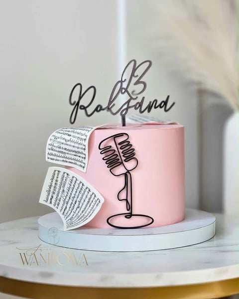 Pink podcast-themed cake with microphone design and sheet music, displayed on white platform with Rockland logo