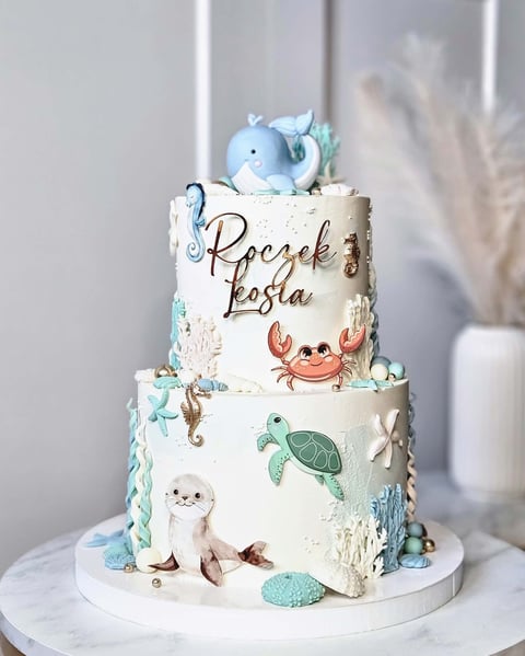 Two-tiered ocean-themed cake with blue elephant topper, sea turtle and otter decorations, and Roczek Losla text on white frosting