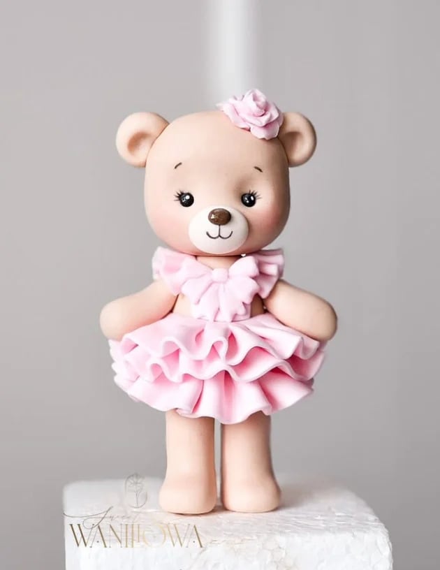 Cute decorative bear figurine wearing a pink ruffled dress and flower headpiece on a white base