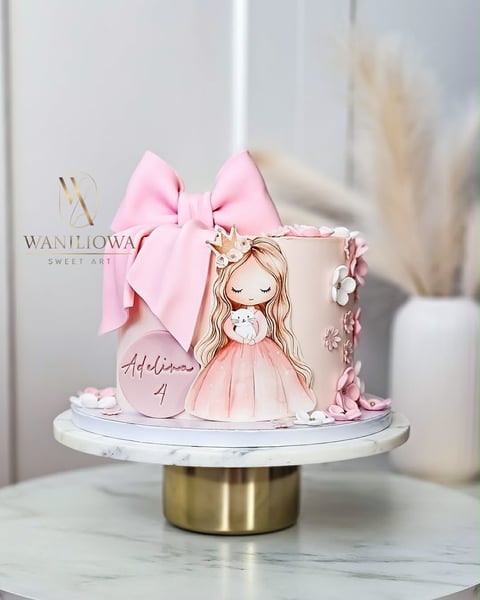 Pink and white tiered cake decorated with illustrated girl figure, large pink bow, and personalized text on marble pedestal stand