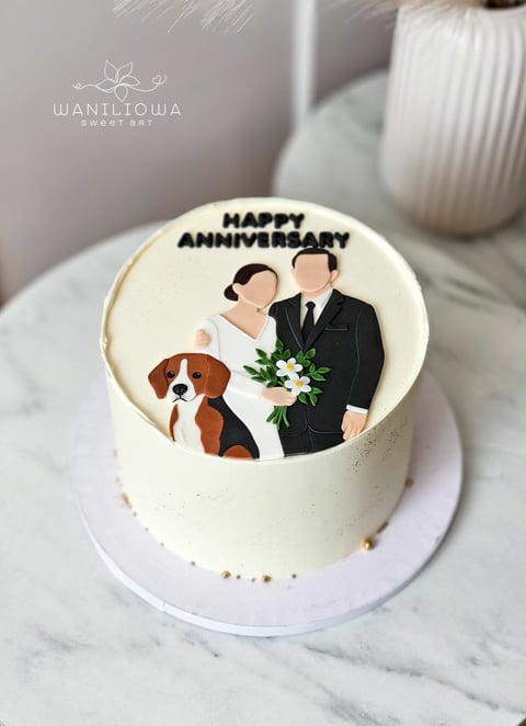 White anniversary cake decorated with an illustration of a couple with a dog, fresh flowers, and happy anniversary text