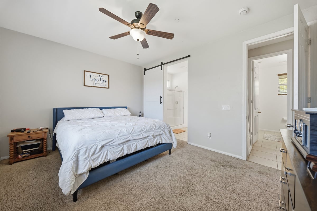 Modern bedroom with blue upholstered bed, ceiling fan, and en-suite bathroom door visible