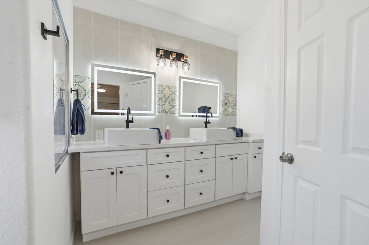 Modern bathroom with white double vanity, illuminated mirrors, and dual sinks with black fixtures