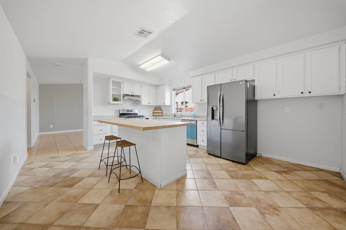 Modern kitchen with white cabinetry, stainless steel refrigerator, wooden countertop island with bar seating, and tile flooring